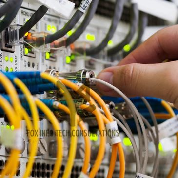 Hand connecting cables to a network switch with glowing status lights.
