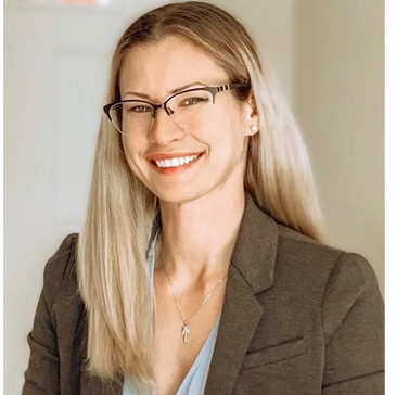 Smiling woman with glasses wearing a blazer and necklace.