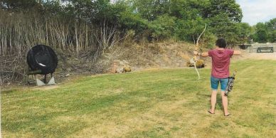 A person practicing archery outdoors with a bow and target.
