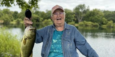 Elderly man joyfully holding a large fish by a lake.