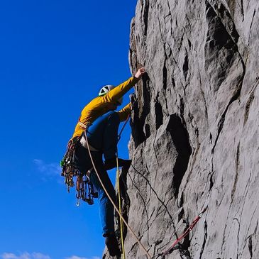 A climber in a yellow jacket ascending a steep rock face.