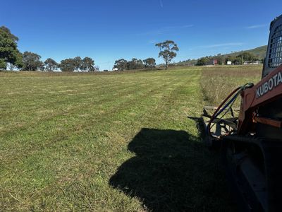 A Kubota tractor working on a mowed grassy field under a clear blue sky.