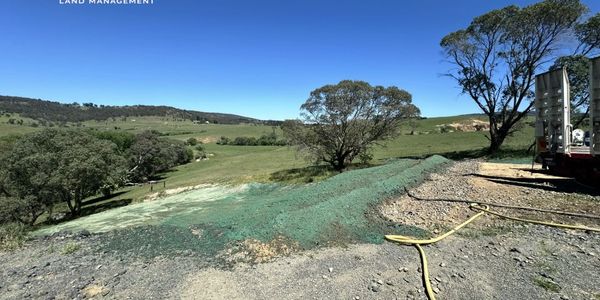 A rural landscape with trees, green hills, and construction equipment under a clear blue sky.