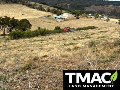 Rolling hills with dry grass and a distant farmhouse under a cloudy sky.