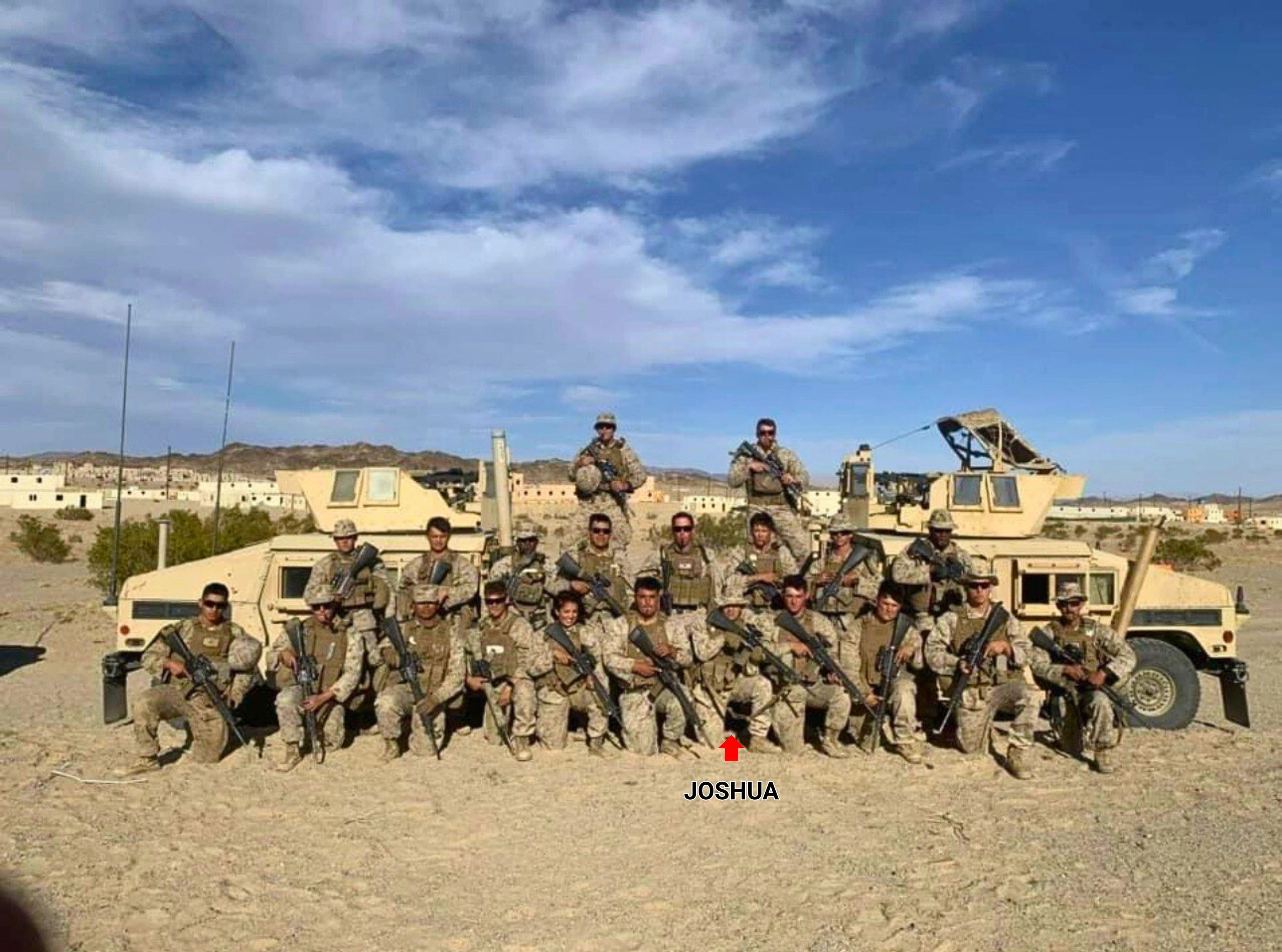 Military group photo with soldiers and vehicles in desert terrain under a blue sky.