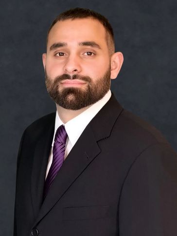 Man in a black suit and purple tie posing against a dark background.