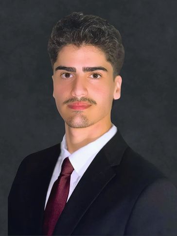 Young man in a suit with a maroon tie and white shirt against a dark background.