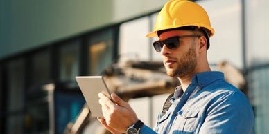 Construction worker in a hard hat using a tablet outdoors.