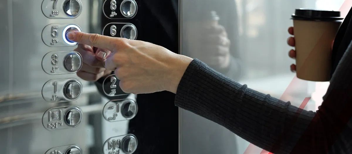 Person pressing elevator button while holding a coffee cup.