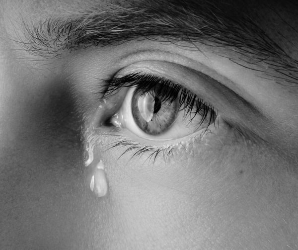A black and white image of an eye with a tear  drop.