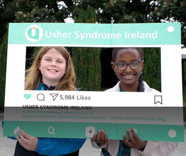 Two girls posing together while holding up a large cardboard cutout shaped like an Instagram frame.