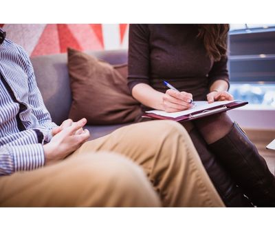 Two people are sitting and one is writing on a notepad.