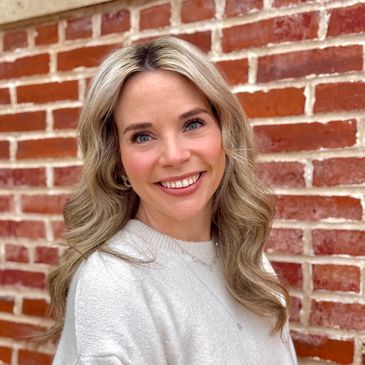 Smiling woman with blonde hair against a brick wall.