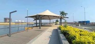 A shaded pavilion beside a waterfront with greenery and a wooden walkway.