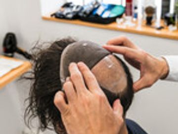 Person fitting a hairpiece on balding head.