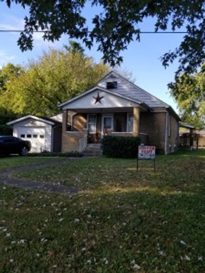 A small brick house with a star decoration and a 'For Sale' sign in the yard.