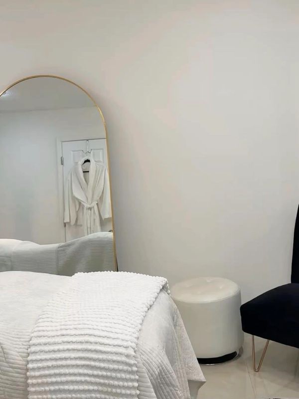 Minimalist bedroom with a bed, mirror, chair, and robe.