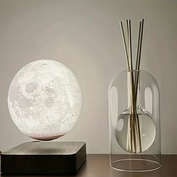 A levitating moon lamp beside a modern glass vase with sticks.