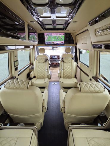 Luxurious van interior with cream leather seats and a ceiling TV.