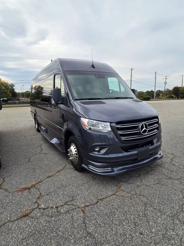 A dark gray Mercedes-Benz Sprinter van parked on cracked asphalt under a cloudy sky.
