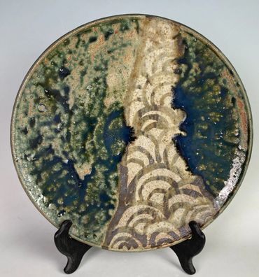 Handcrafted ceramic plate with abstract glaze and wave patterns on display stand.