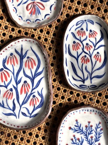 Hand-painted ceramic dishes with floral designs on woven surface.