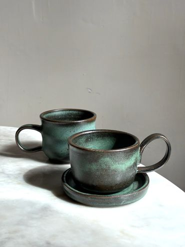 Two rustic green ceramic cups on a white marble surface.