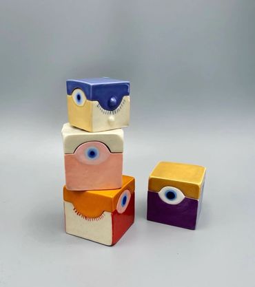 Colorful ceramic cubes with eye designs stacked on a gray surface.
