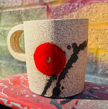 Speckled ceramic mug with bold red flower design on a colorful surface.
