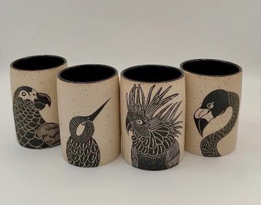 Set of ceramic cups with black bird illustrations on beige background.
