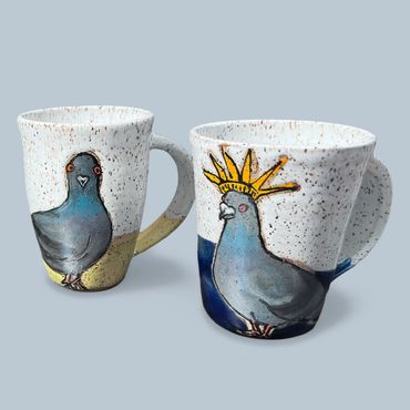 Two ceramic mugs featuring hand-painted pigeons, one with a crown.