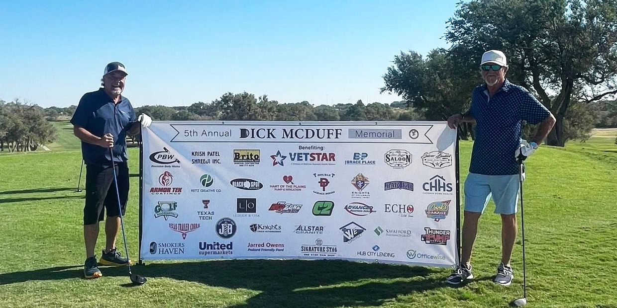 Two men holding a banner at a golf event on a sunny day.
