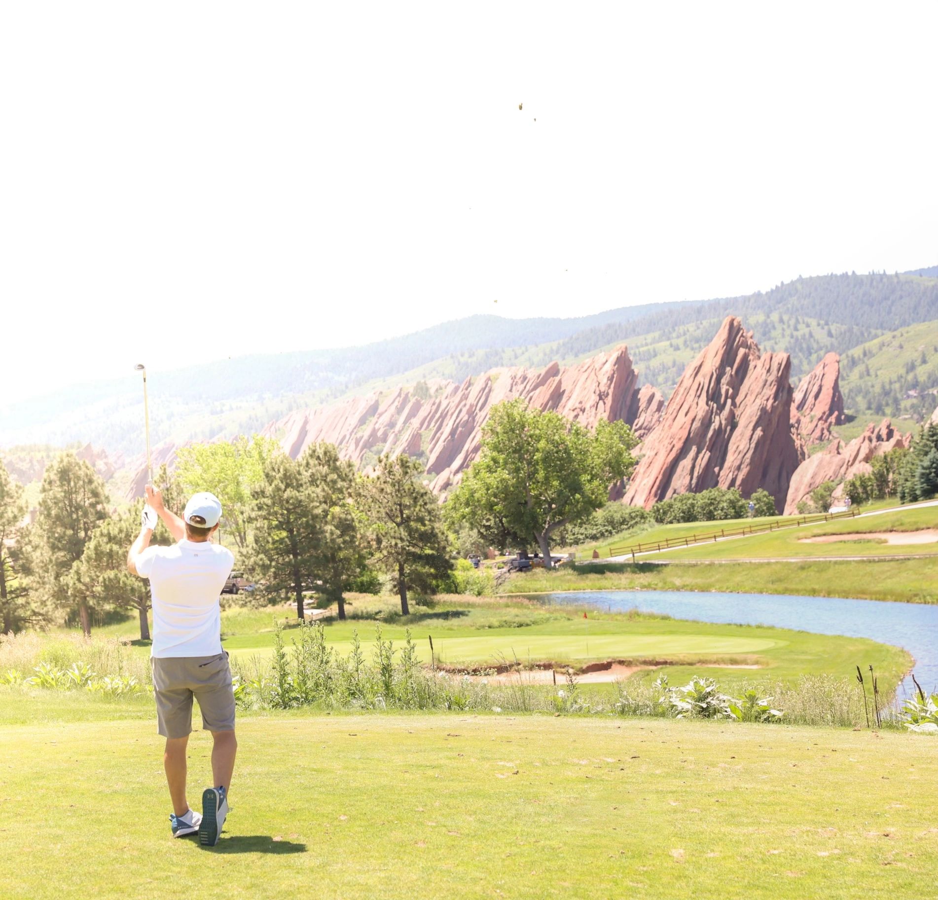 Golfer in white shirt swings on a scenic course with towering red rocks.