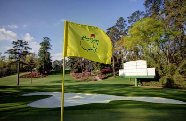 Yellow Masters golf flag on a scenic green course with sand trap.