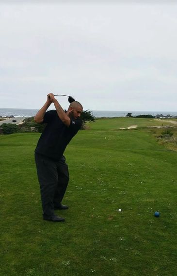 Man in black preparing to swing golf club on a coastal golf course.