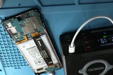 Disassembled Samsung phone connected to a charging device on a blue mat.