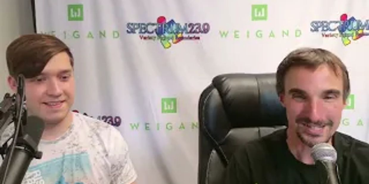 Two men sitting with microphones, smiling.
