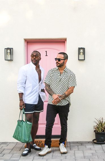 Two stylish men standing in front of a pink door, showcasing casual summer fashion.