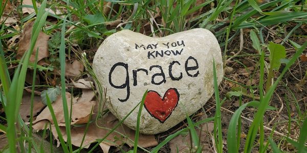 Heart-shaped rock with message 'May you know grace' and a red heart.