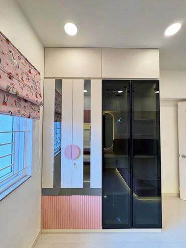 Modern wardrobe with pink, white, and black glass doors under ceiling lights.