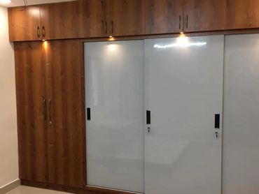 Modern wooden wardrobe with white sliding doors and built-in spotlights.