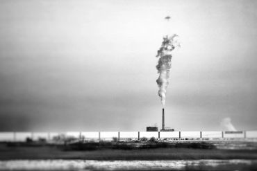 Industrial chimney emitting smoke in a desolate landscape.