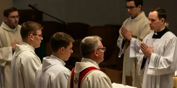 A group of priests and altar servers in white robes during a religious service.