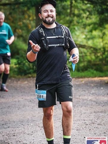 Smiling runner in black athletic wear during a race with a water bottle in hand.