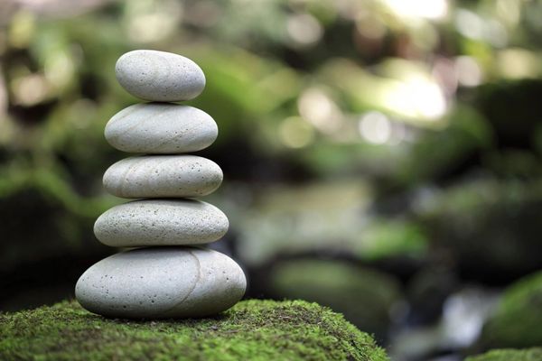 A stack of five grey and tan rocks is balanced on a light sandy surface with a blurred background.