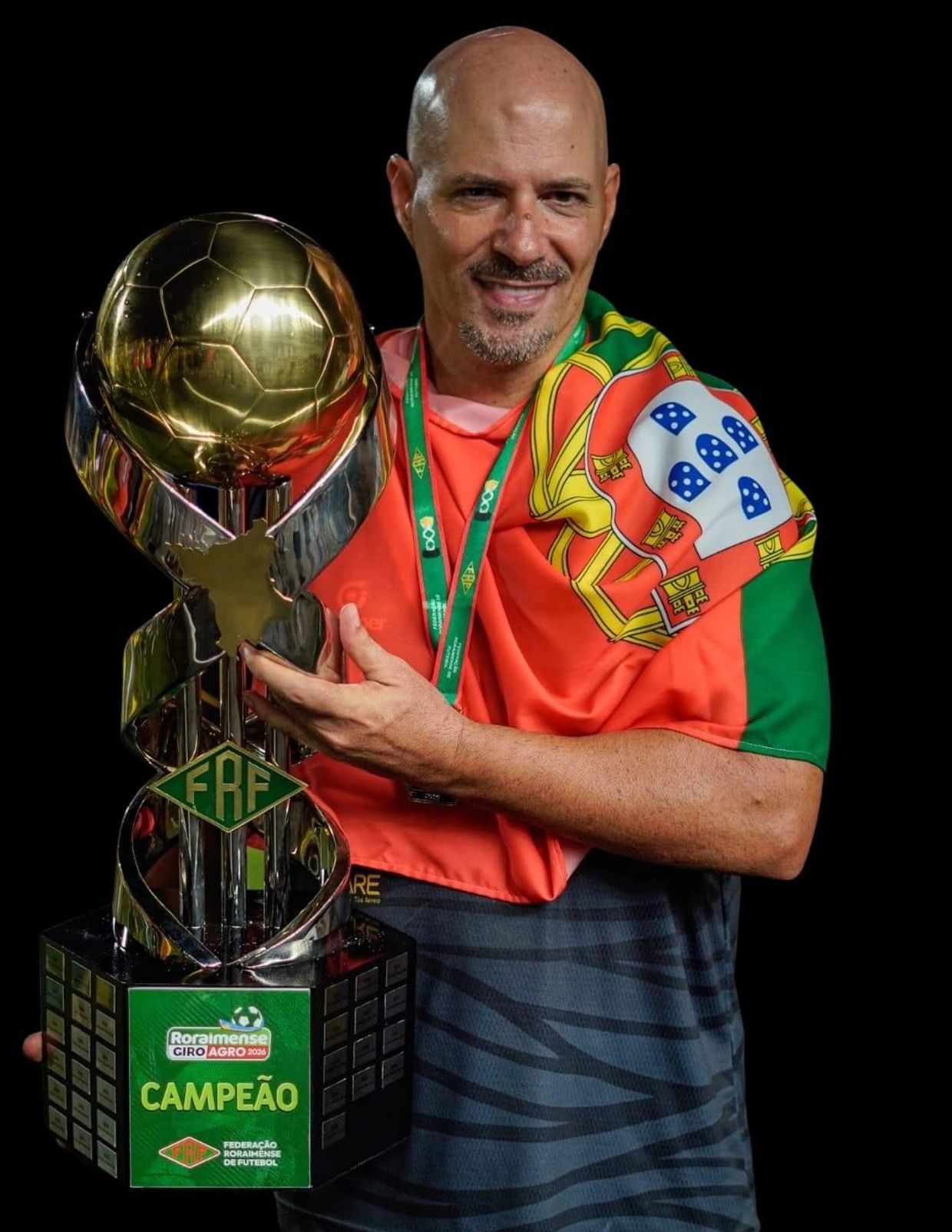Man wrapped in Portuguese flag holding a large football trophy with 'Campeão' label.
