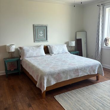 Minimalist bedroom with a wooden bed, light bedding, teal nightstands, and a ceiling fan shaped like leaves.