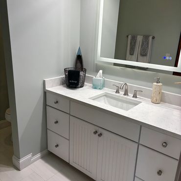 Modern bathroom vanity with white cabinets and illuminated mirror.