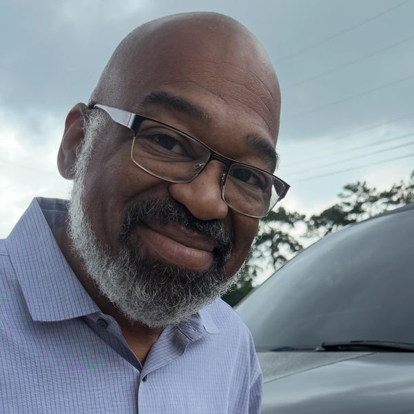 Smiling man holding a book titled 'Faith Manor' by Frank Thompson Jr.