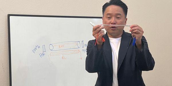 A man explains a concept using a pen in front of a whiteboard with diagrams.